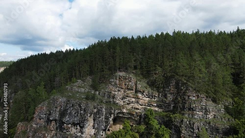 Rocky coast of a mountain river. Picturesque steep slope covered with coniferous forest. Majestic epic northern nature. Cinematic landscape from drone. Smooth camera movement from a group of tourists