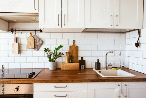 Kitchen brass utensils, chef accessories. Hanging kitchen with white tiles wall and wood tabletop.Green plant on kitchen background 