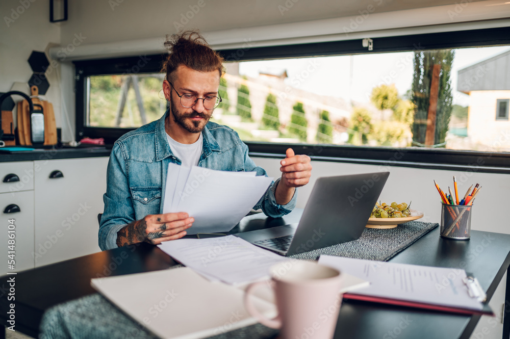 Young business man working at home with laptop and papers on desk Young business man working at home with laptop and papers on desk