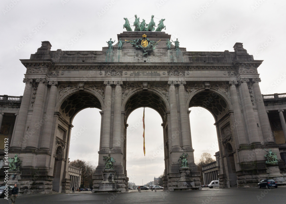 Cinquantenaire Park Arc with quadriga bronze sculpture at the top of the scructure with belgium flag and cloudy sky at background 