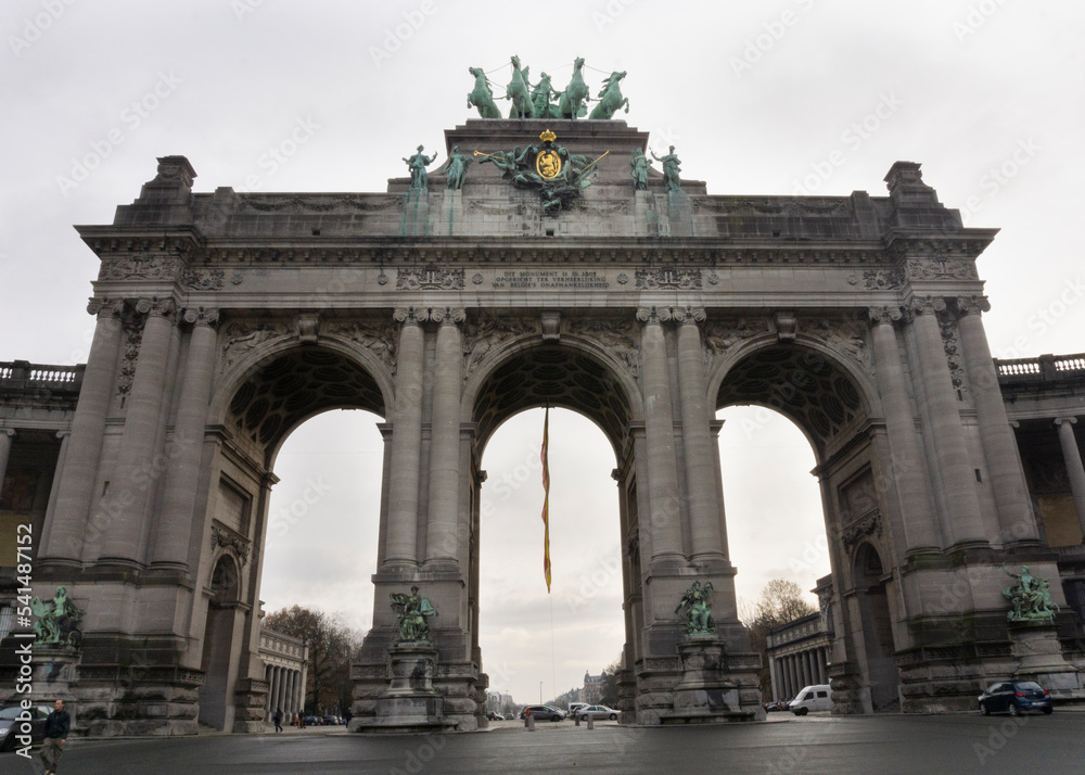 Cinquantenaire Park Arc with quadriga bronze sculpture at the top of the scructure with belgium flag and cloudy sky at background Cinquantenaire Park Arc with quadriga bronze sculpture at the top of the scructure with belgium flag and cloudy sky at background