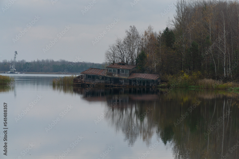 Pripyat Rusty and destroyed boat house with autumn forest and grey cloudy sky at background