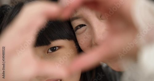 closeup with selective focus asian girl and mother showing love sign with hands. they look through fingers with smiles