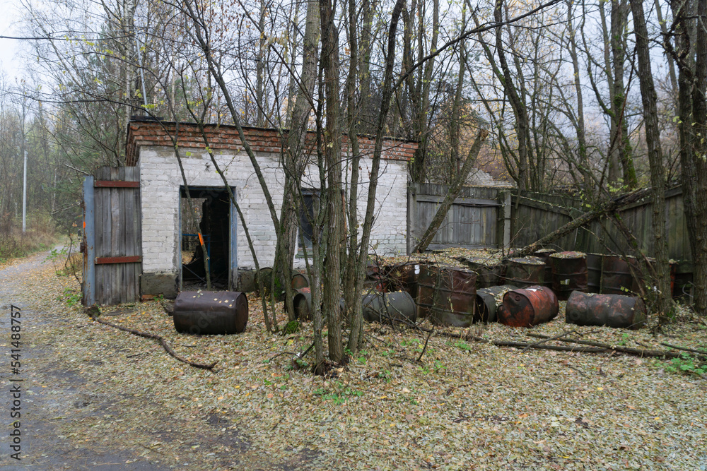 Rusty and corroed oil barrels over ground in front of a small white abandonated storage at chernobyl nuclear disaster exclusion zone Rusty and corroed oil barrels over ground in front of a small white abandonated storage at chernobyl nuclear disaster exclusion zone