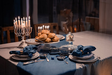 Food for Hanukkah celebration: Menorah Candles on wooden table, sufganiyot cake and table setting, jewish symbol centerpieces, white and blue. holiday Israel hebrew traditional family celebration
