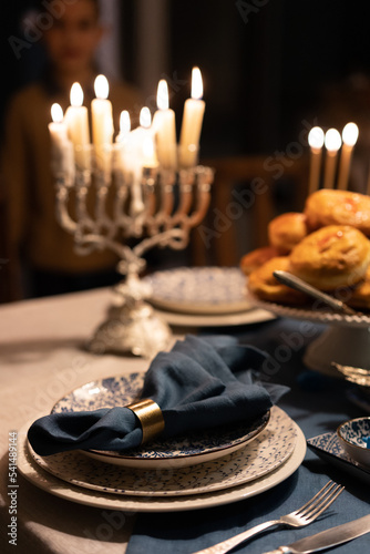 Food for Hanukkah celebration: Menorah Candles on wooden table, sufganiyot cake and table setting, jewish symbol centerpieces, white and blue. holiday Israel hebrew traditional family celebration photo