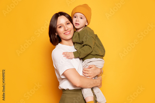 Happy young mother with her cute little son posing isolated on bright yellow background. Family, love, motherhood and Mother's day concept