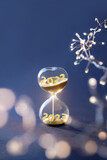 End of the year 2022, Silverster, Happy New Year 2023. Hourglass with numbers 2022 and 2023 and light garland on dark blue background. Hourglass is also known as sandglass, sand glass, sand timer or