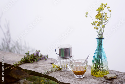 Vietnamese filter coffee on a wooden bench with wild flowers in winter weather
