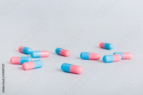 Heap of pink and blue pills on colored background. Tablets scattered on a table. Pile of red soft gelatin capsule. Vitamins and dietary supplements concept