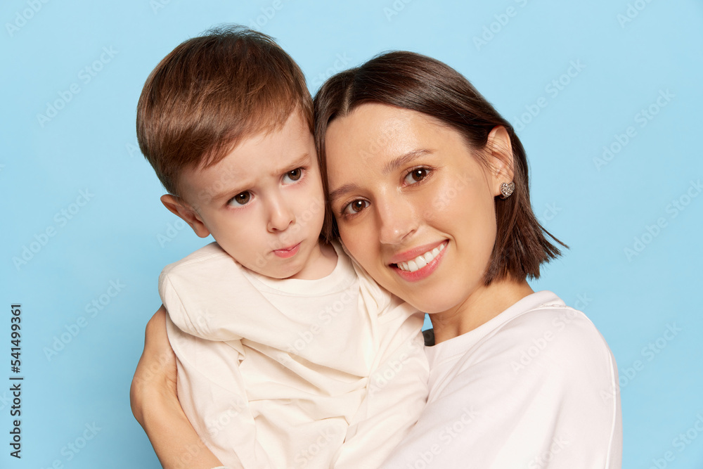 Tenderness. Young beautiful happy woman hugging her little son, kid isolated on blue background. Family, love, motherhood and Mother's day concept Tenderness. Young beautiful happy woman hugging her little son, kid isolated on blue background. Family, love, motherhood and Mother's day concept