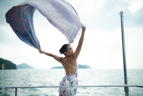 Fotografie An Asian girl on a yacht stand to receive the fresh air from the sea with a shaw