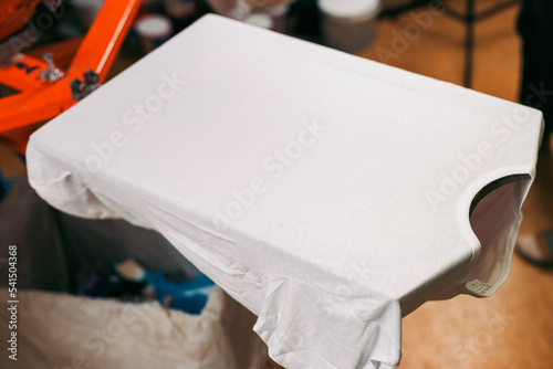 white t-shirt is ready for printing. creating print on t-shirt in workshop. serigraphy production. silkscreen printing selective focus close-up photo