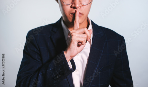 Photo closeup of Business man wearing classic costume looking on camera and holding index finger on lips isolated over white background.