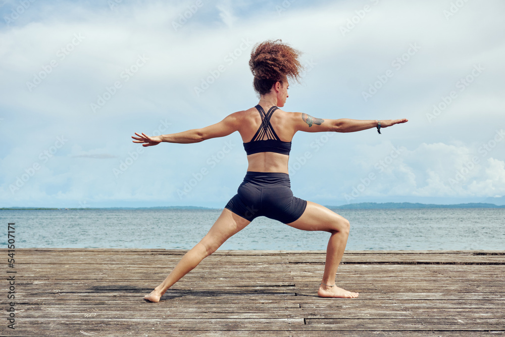 Female practicing Warrior asana on tropical shore quay Female practicing Warrior asana on tropical shore quay
