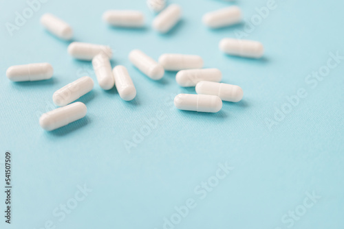 White capsule pills on blue background with copy space. Medicine and health concept.