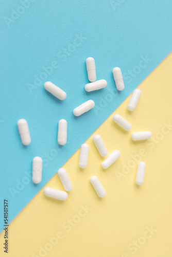 White pills on a yellow and blue pastel background. Capsules pills close-up. health care and medicine. 