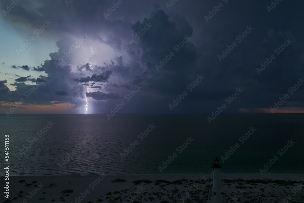 White tall lighthouse on sea shore with blinking light at stormy night