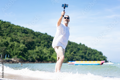  Man taking selfie of himself after workout. Good looking taking a self-portrait picture with his smartphone camera on a beach during summer vacation travel.