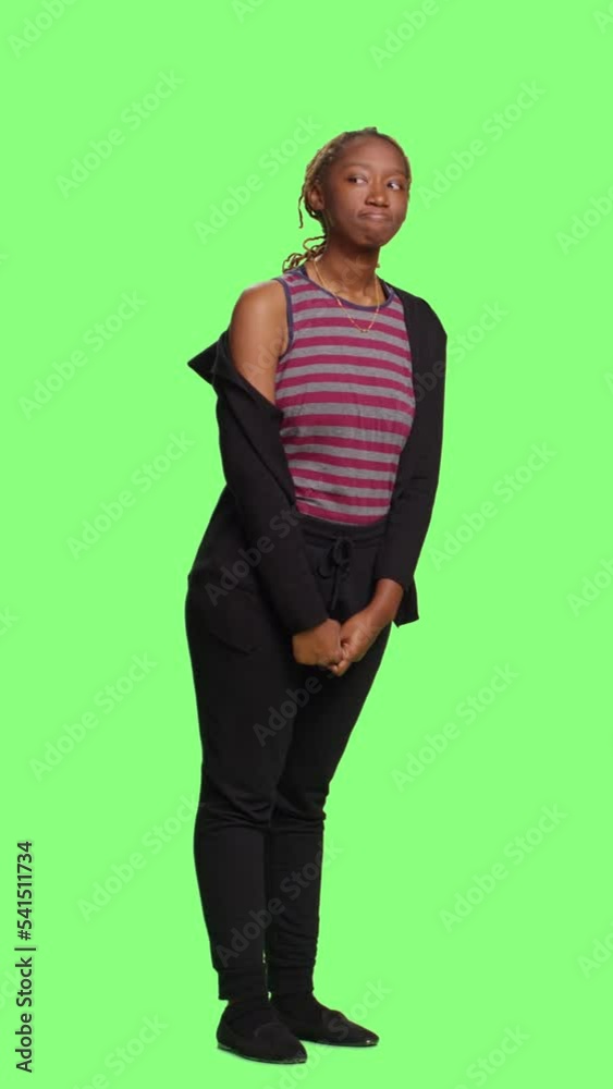 Vertical video: African american girl standing on full body green screen backdrop, waiting in line. Impatient joyful adult wait and acting curious, modern confident person over greenscreen background.