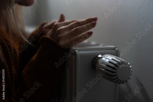 Woman warming her hands on the heater, close-up. Hands and heater radiator as cold winter concept.