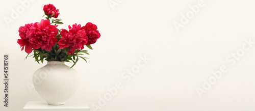 Purple pion flower bouquet in white vase on gray beige interior wall. Minimalist still life. Light and shadow nature background. photo