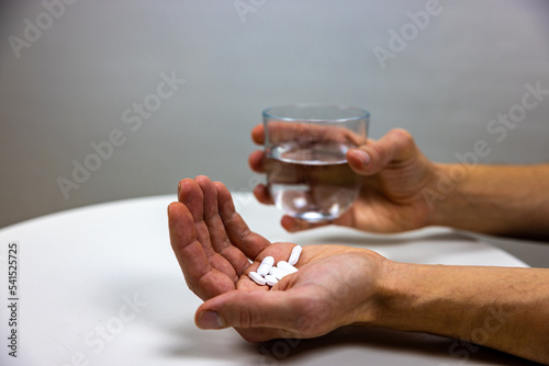 A ´photo showing a hand with pills and another hand holding a glass of water. Painkillers. Antidepressants. Addicted to drugs. Healthcare. Social problems. Morphin problem.