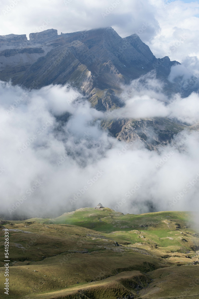 Montain hut with lush meadows in the French Pyranees surrounded by clouds with the Breche de Roland in the background