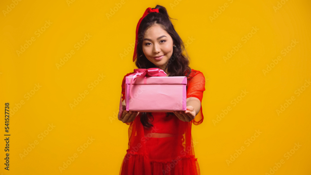 joyful young asian woman holding wrapped present isolated on yellow joyful young asian woman holding wrapped present isolated on yellow