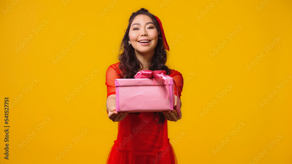 positive and young asian woman giving wrapped present isolated on yellow positive and young asian woman giving wrapped present isolated on yellow