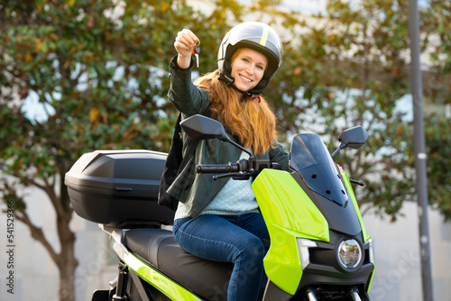 Red-haired woman riding a motorcycle on a city street showing the keys