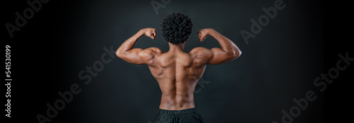 Sportsman showing his back muscles. Athlete flexing muscles. Black background.