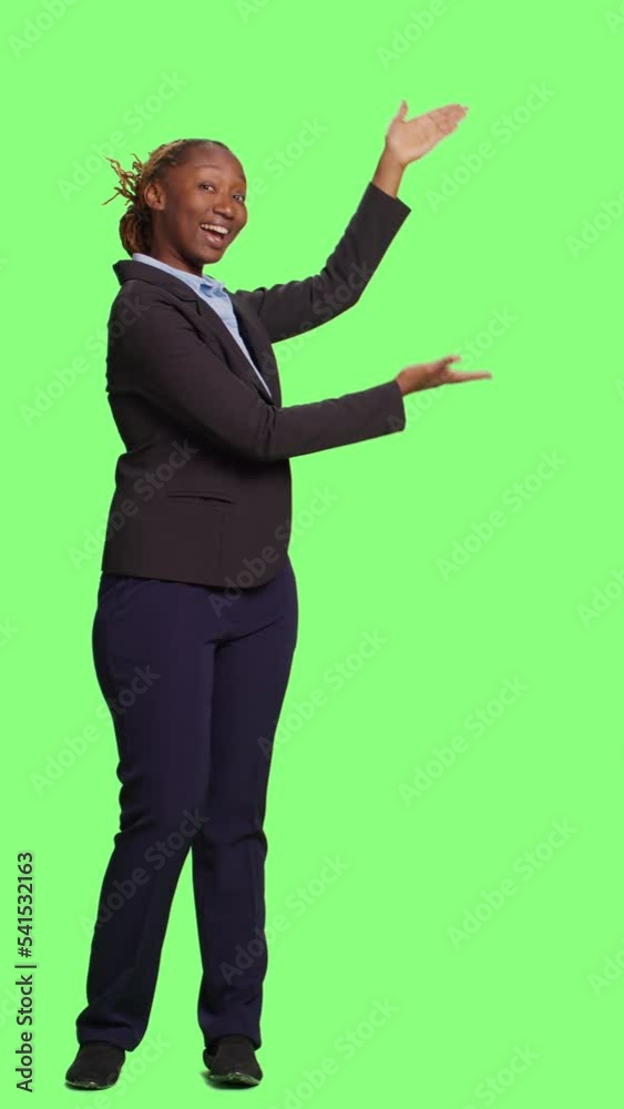 Vertical video: African american businesswoman doing green screen advertisement over full body greenscreen backdrop. Female manager showing ad example and promotion on studio background, smiling adult Vertical video: African american businesswoman doing green screen advertisement over full body greenscreen backdrop. Female manager showing ad example and promotion on studio background, smiling adult