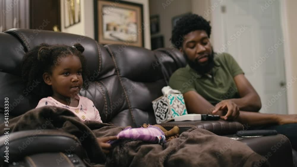 Black African-American father relaxing at home on couch in living room with Black daughter at home Black African-American father relaxing at home on couch in living room with Black daughter at home