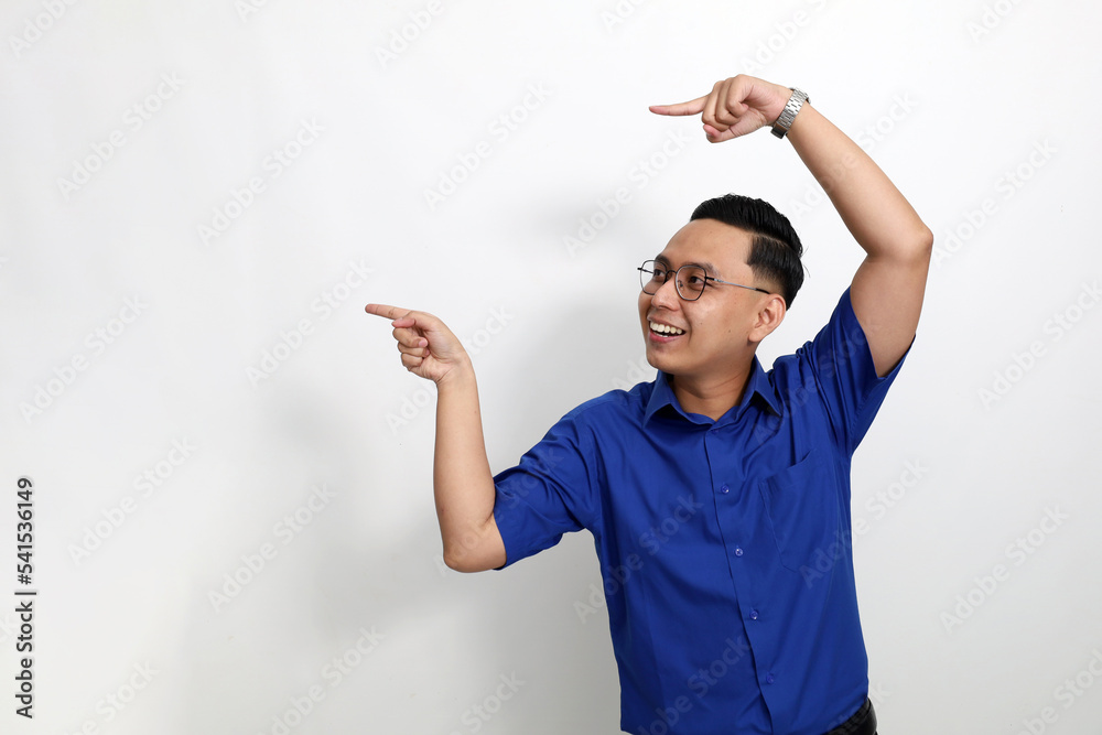 Excited young asian man standing while pointing or presenting something on blank space beside him. Isolated on white