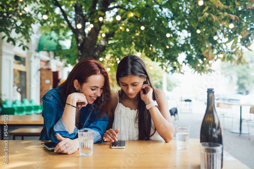 Two female friends browsing in mobile phones at street cafe. photo