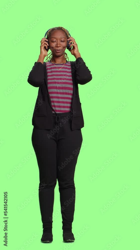 Vertical video: Modern person enjoying music on audio headset, standing full body on green screen backdrop. Listening to mp3 radio songs and sounds on wireless headphones, acting cheerful. Vertical video: Modern person enjoying music on audio headset, standing full body on green screen backdrop. Listening to mp3 radio songs and sounds on wireless headphones, acting cheerful.