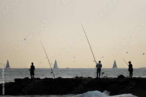 silhouette of fishermen with sailboats in the distance in the sunset