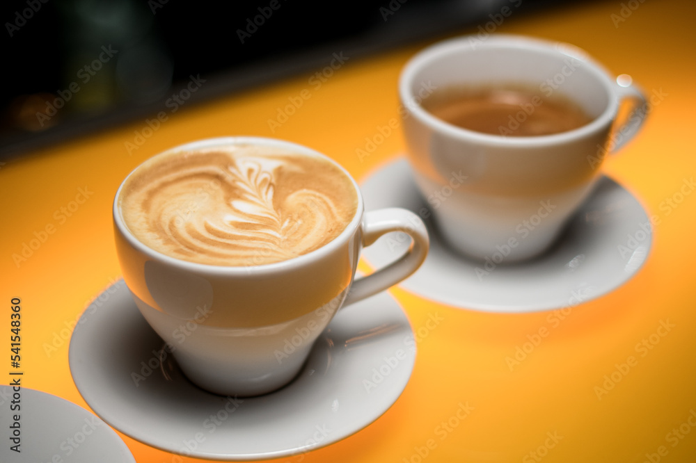 close-up view on white cup with tasty coffee drink with saucer on yellow table close-up view on white cup with tasty coffee drink with saucer on yellow table