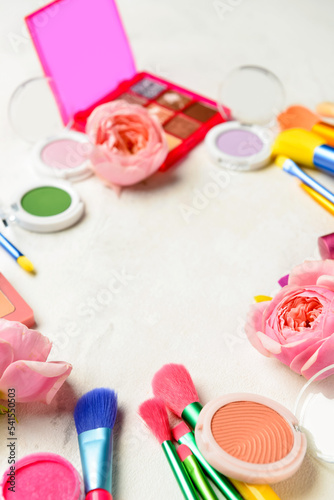 Decorative cosmetics, brushes and flowers on light background