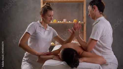 Two masseurs work simultaneously on the patient back, 4 hands massage, effective therapeutic massage. Woman enjoying a relaxing massage at spa treatment. photo