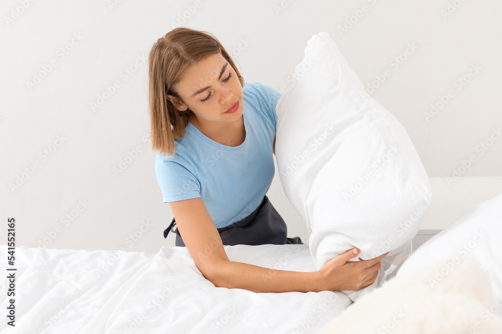 Young housewife adjusting pillow in bedroom Young housewife adjusting pillow in bedroom