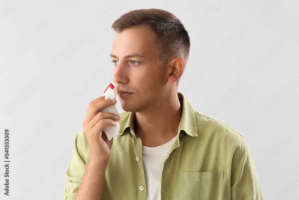Young man with nosebleed and tissue on white background, closeup Young man with nosebleed and tissue on white background, closeup