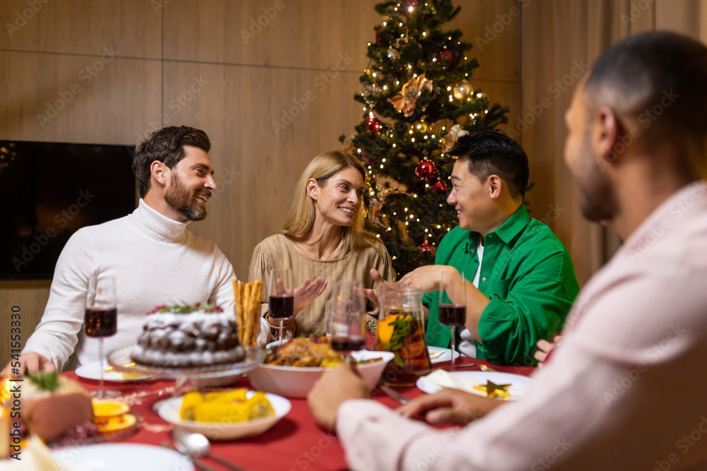 Working corporate. A company of young, beautiful, interracial people are celebrating a New Year's corporate party. They are sitting at the festive table near the Christmas tree, talking, laughing. Working corporate. A company of young, beautiful, interracial people are celebrating a New Year's corporate party. They are sitting at the festive table near the Christmas tree, talking, laughing.