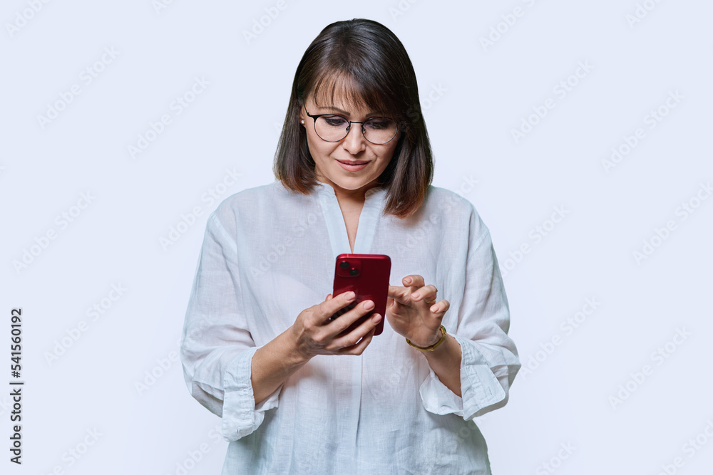 Middle aged focused woman using smartphone on white studio background. Middle aged focused woman using smartphone on white studio background.