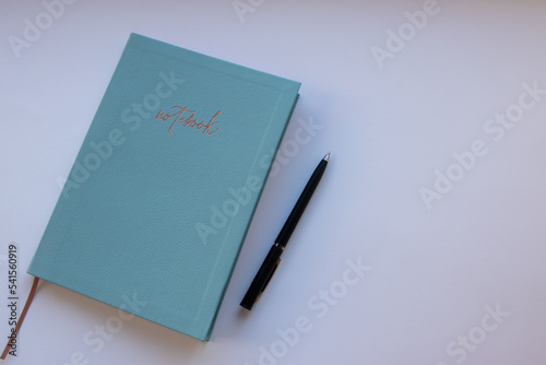 Notebook with pen on white background. Stationery minimalist still life. Notebook with blue cover and black pen on table workspace. Top view, flat lay, copy space