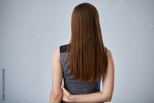 Woman with long hair standing back on gray isolated background.
