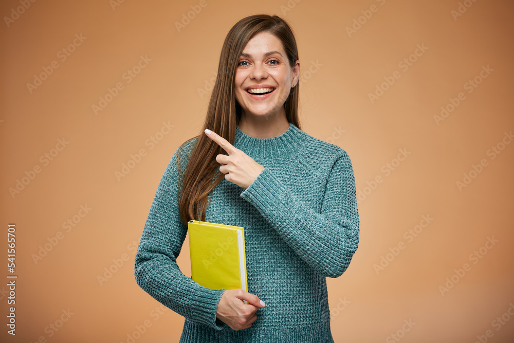 Woman in warm clothes holding yellow book and pointing finger up. Advertising female studio portrait on orange back. Woman in warm clothes holding yellow book and pointing finger up. Advertising female studio portrait on orange back.