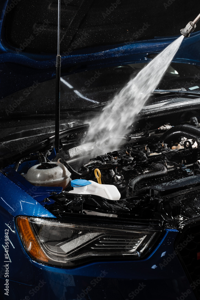 Pouring water on car engine. Washing car engine with spray, brush and