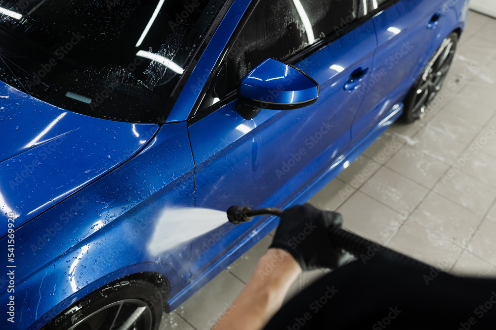 Car washer pouring water for full body car wash. Spraying water on car to wash off foam in the garage. Process of detailing washing in car service. Car washer pouring water for full body car wash. Spraying water on car to wash off foam in the garage. Process of detailing washing in car service.